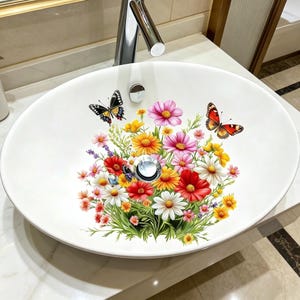 May include: Oval white ceramic bathroom sink with a floral and butterfly design. The sink features a vibrant bouquet of red, pink, yellow, and white flowers, with several butterflies. A chrome tap is visible above the sink.