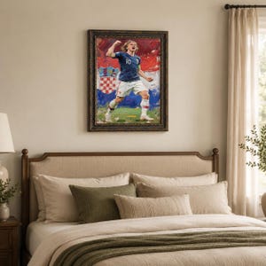 May include: A framed painting of a soccer player in a blue jersey with the number 10, celebrating a goal. The background features the Croatian flag and a green field. The painting is in a dark, ornate frame.