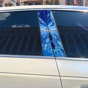Könnte beinhalten: Ein weißes Auto mit einem vertikalen Säulenaufkleber, der eine lebendige Illustration im Anime-Stil zeigt. Die Grafik zeigt eine Figur, die auf einer reflektierenden blauen Wasseroberfläche unter einem hellen Himmel mit einem Torii-Tor steht.