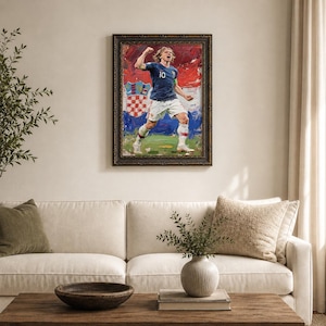 May include: Framed oil painting of a soccer player in a blue jersey with the number 10, celebrating a goal. The background features the Croatian flag. The painting is displayed above a white sofa and wooden coffee table.