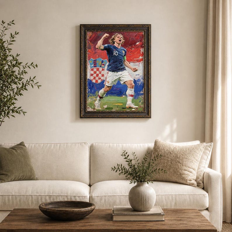 May include: Framed oil painting of a soccer player in a blue jersey with the number 10, celebrating a goal. The background features the Croatian flag. The painting is displayed above a white sofa and wooden coffee table.