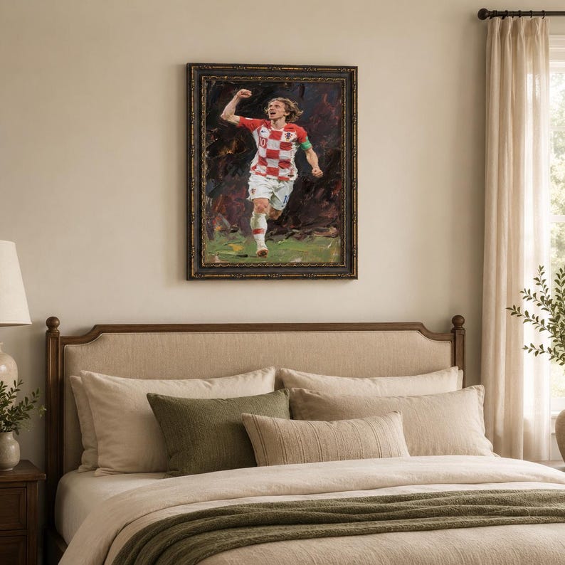 May include: Framed artwork of a soccer player in a red and white checkered jersey, celebrating a goal. The painting has a dark, textured background and a gold-toned frame. The player is running on a green field.