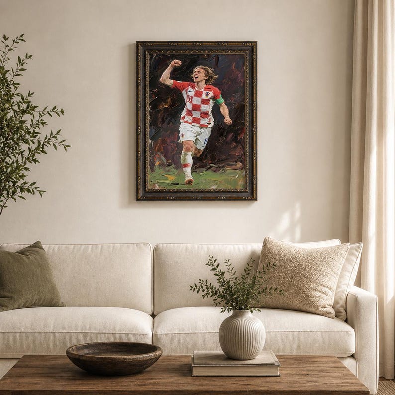 May include: An oil painting of a soccer player in a red and white checkered jersey, framed in a dark ornate frame. The player is running with his arm raised in celebration. The background is dark and abstract, with green and brown tones.