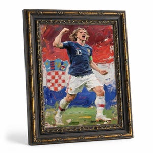 May include: Framed oil painting of a soccer player in a blue jersey with the number 10, celebrating a goal. The background features the Croatian flag and a coat of arms. The frame is black with gold accents.