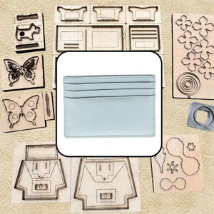 Puede incluir: Un tarjetero de cuero azul claro con una superficie texturizada, que presenta tres ranuras horizontales en la parte frontal para organizar tarjetas. El tarjetero tiene una forma rectangular con bordes cosidos y se muestra sobre un fondo de varios troqueles de corte de metal.