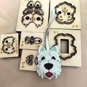 May include: A light blue leather dog-shaped keychain with a black nose and red tongue, displayed alongside several wooden die-cutting molds labeled with numbers like 5-1, 5-2, 5-3, 5-4, and 5-5, used for crafting the individual components of the keychain.