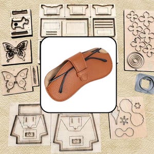 May include: A tan, textured leather spectacle case with a central strap closure, containing a pair of black-framed spectacles. The case is surrounded by various wooden cutting dies featuring shapes like butterflies, flowers, and geometric patterns.