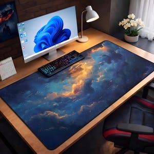 May include: A large rectangular desk mat with a celestial design featuring blue, gold, and white clouds. The mat is placed on a wooden desk, with a computer monitor, keyboard, and desk lamp visible.