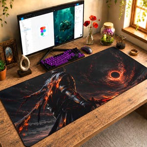 May include: A large black and red gaming mouse pad featuring a fantasy warrior design. The pad has a dark background with a fiery, swirling pattern and a central circular element. A computer monitor, keyboard, and other desk accessories are visible.