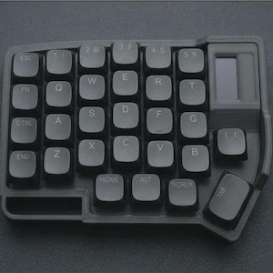 Könnte beinhalten: Eine schwarze ergonomische Tastatur mit kompaktem Design. Die Tastatur verfügt über eine Vielzahl von Tasten, darunter Buchstaben, Zahlen und Funktionstasten. Sie hat einen kleinen Bildschirm und ein einzigartiges Layout für effizientes Tippen.