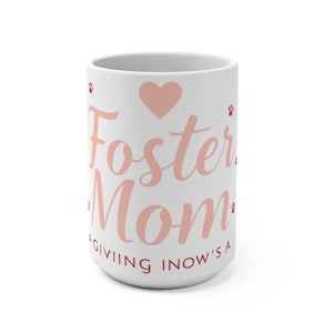 Peut inclure: Mug en céramique blanche avec l'inscription "Foster Mom" en rose, un cœur rose et des empreintes de pattes. Le bas de la tasse porte l'inscription "Giving now's a". Un cadeau pour une famille d'accueil.