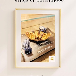 May include: Framed artwork with a cast of hands and baby feet. The hands are gold and blue, holding the baby feet. The text "wings of parenthood" is at the top, with "Yash Us We" and other text below. The artwork is in a light-coloured frame.