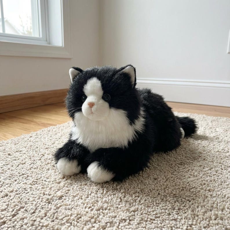May include: A plush, black and white cat toy with a soft, fluffy texture. The toy cat is lying down on a beige carpet, with its paws and face in white and the rest of its body in black.