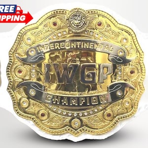 May include: A gold-plated championship belt featuring a large central plate with the text IWGP INTERCONTINENTAL CHAMPION, intricate filigree engravings, embedded red stones, and clear crystals, attached to a wide white leather strap.