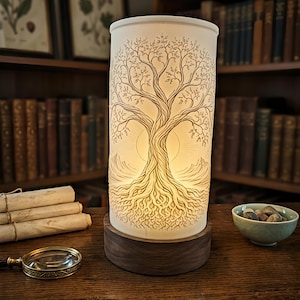 Può includere: Una lampada cilindrica in vetro smerigliato con un dettagliato disegno a linee nere di un albero con radici e rami estesi. La lampada è illuminata dall'interno e poggia su una base circolare in legno scuro.