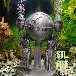 May include: A silver-colored aquarium decoration featuring a globe with the text "THE WORLD IS YOURS" and two female figures holding urns. The decoration is in an aquarium with a fish and the text "STL FILE".