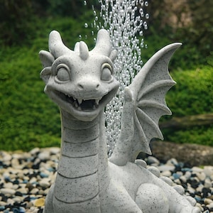 May include: A smiling, light gray dragon statue with wings, horns, and a long neck. The dragon is sitting on a bed of small rocks, with water bubbles rising in the background. The statue is likely for an aquarium.