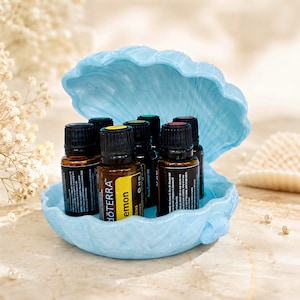 Peut inclure: Un récipient bleu clair en forme de coquillage contenant six petits flacons d'huile essentielle en verre ambré avec des bouchons noirs. Une étiquette jaune avec le texte "dōTERRA" et "lemon" est visible sur l'un des flacons.