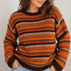 May include: A long-sleeved crochet sweater featuring horizontal stripes in shades of dark brown, burnt orange, bright orange, and beige. The garment has a round neckline and ribbed cuffs and hem in a solid dark brown color.