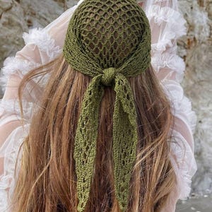 May include: An olive green crochet head covering with a net-like design. The head covering is tied at the nape of the neck with long, openwork ties. The head covering is shown on a person with long, light brown hair.