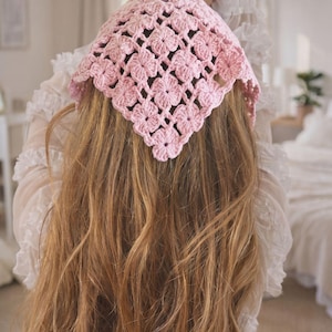 May include: A light pink crocheted headscarf with a floral pattern. The head covering is square-shaped and covers the top of the head. The scarf is made of a soft, textured yarn.