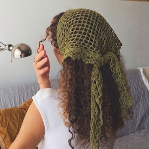 May include: A green crocheted head covering with a net-like design. The head covering is tied at the back and drapes down the back of the head. The person in the image is wearing a white top.