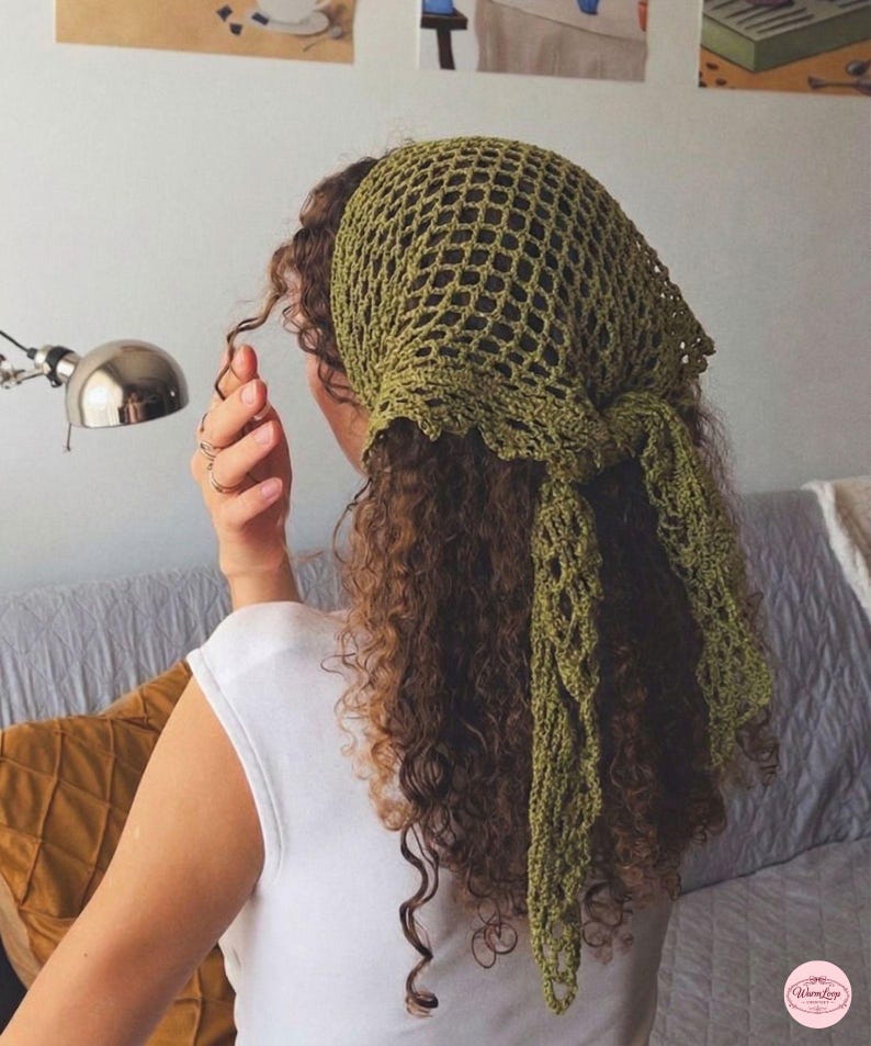May include: A green crocheted head covering with a net-like design. The head covering is tied at the back and drapes down the back of the head. The person in the image is wearing a white top.