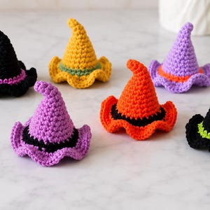 May include: Six small crocheted witch hats in various colors including black with purple, yellow with green, purple with orange, orange with black, purple with black, and black with lime green. Each hat features a pointed top and a wavy brim.