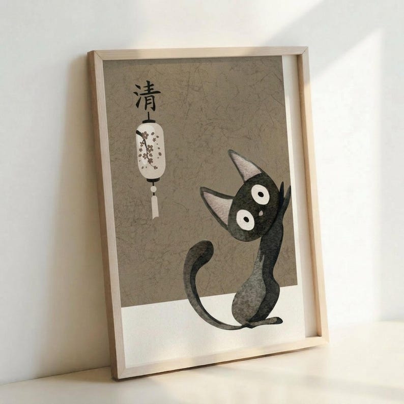 May include: Framed poster print leaning against white wall showing minimalist illustration of black cat character with large white eyes sitting beside white paper lantern with cherry blossom design and Japanese characters above on textured beige background, displayed in light wooden frame