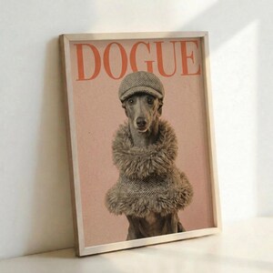 May include: Framed poster print leaning against white wall showing a whippet or greyhound wearing a herringbone flat cap and furry brown coat against a pink background, with "DOGUE" text in orange letters at top, displayed in light wooden frame on white surface