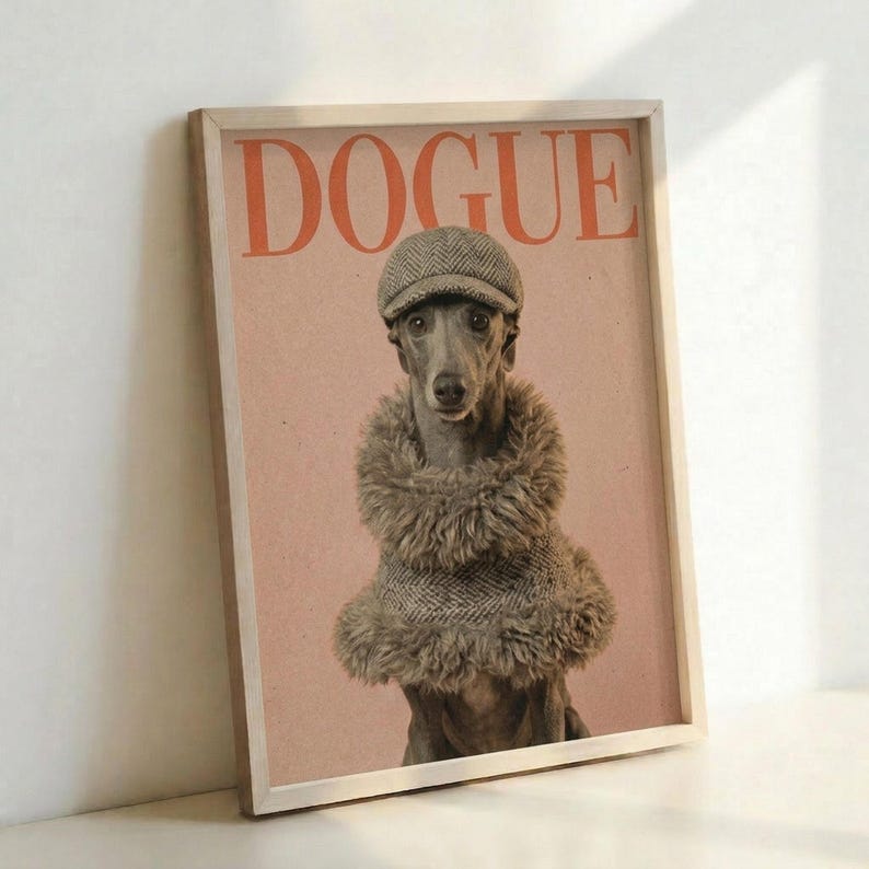May include: Framed poster print leaning against white wall showing a whippet or greyhound wearing a herringbone flat cap and furry brown coat against a pink background, with "DOGUE" text in orange letters at top, displayed in light wooden frame on white surface