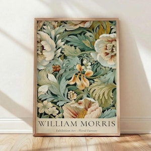 May include: A framed art print featuring a floral design in shades of cream, green, and gold. The artwork, by William Morris, showcases intricate botanical patterns with a vintage aesthetic. The print is displayed on a wooden floor against a white wall.
