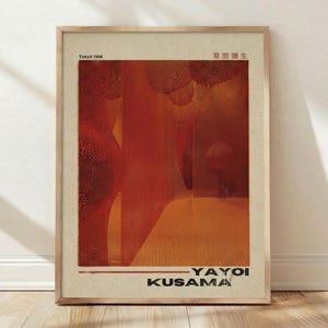 May include: Framed art print featuring an abstract composition in shades of red and orange. The artwork includes the text "Tokyo 1998" and Japanese characters at the top, with "YAYOI KUSAMA" at the bottom. The print is in a light wood frame.