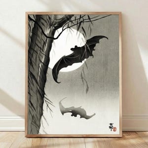 May include: A framed wall art print featuring a black ink wash illustration of a bat flying in front of a large white full moon. A dark tree trunk with hanging branches is on the left side. Japanese characters and a red seal are in the bottom corner.