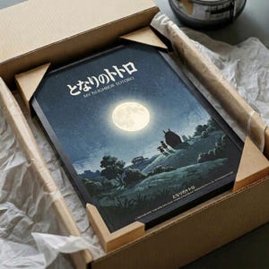 May include: Framed poster showing moonlit nighttime scene with full moon, starry sky, and silhouetted landscape featuring trees and small figures. Japanese text at top reads "My Neighbor Totoro." Art print nestled in cardboard shipping box with protective tissue paper wrapping. Dark blue and teal color palette with cream moon creating atmospheric lighting across rolling hills and vegetation.
