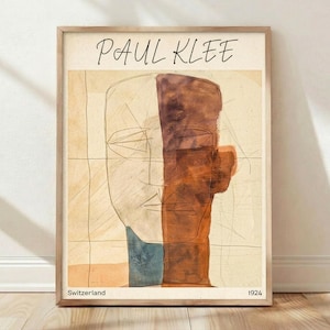 May include: Framed art print featuring a colorful abstract portrait. The artwork, by Paul Klee, has a beige background with a brown and orange face. The text "Paul Klee" is at the top, with "Switzerland" and "1924" at the bottom.