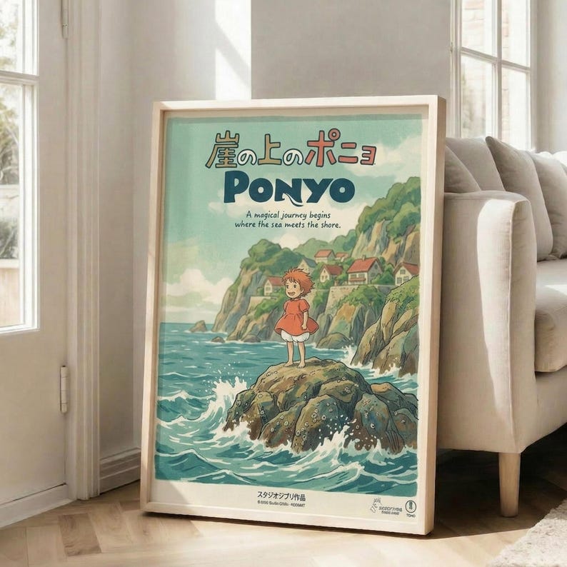 May include: Framed Ponyo movie poster leaning against white wall next to beige sofa in bright living room. Poster shows red-haired girl in orange dress standing on rocky outcrop surrounded by ocean waves, with coastal cliffs and houses in background. Features Japanese text at top, "PONYO" in large letters, and tagline about magical journey. Artwork has vintage travel poster aesthetic with soft watercolor-style illustration in blues, greens, and earth tones.