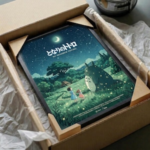 May include: Framed poster print in cardboard box with protective wrapping. Artwork shows nighttime scene with two children standing near large gray forest creature under starry sky with crescent moon. Green hills, trees, and small house visible in background. Warm yellow lights scattered throughout scene. Japanese text at top. Print appears to be in black frame nestled in brown shipping box with white tissue paper padding.