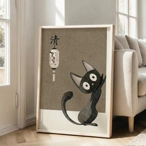 May include: Framed poster print featuring a stylized black cat with large white eyes and pointed ears sitting beneath a white paper lantern with floral details, with Japanese characters above. The artwork has a textured beige and cream background with a cracked vintage appearance. The wooden frame leans against a light gray wall next to a beige upholstered sofa in a bright, minimalist living room with white window trim and natural lighting.