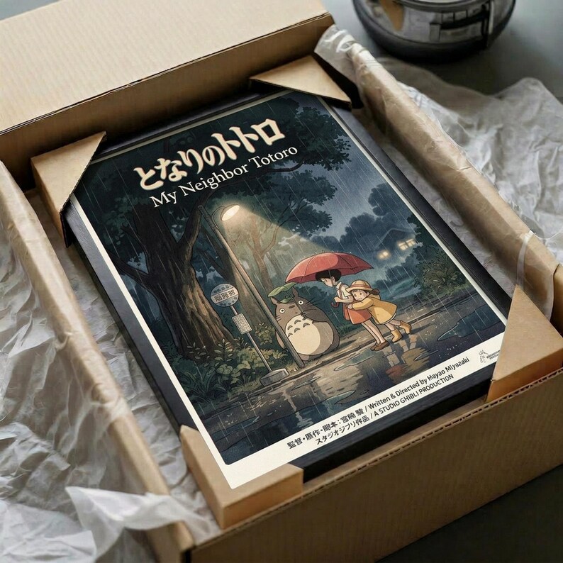 May include: Studio Ghibli My Neighbor Totoro poster print featuring iconic characters under red umbrella in rainy forest scene with bus stop sign. Dark teal and green artwork with Japanese text shown in unboxing scene with brown cardboard packaging, white tissue paper, and wooden desk surface.