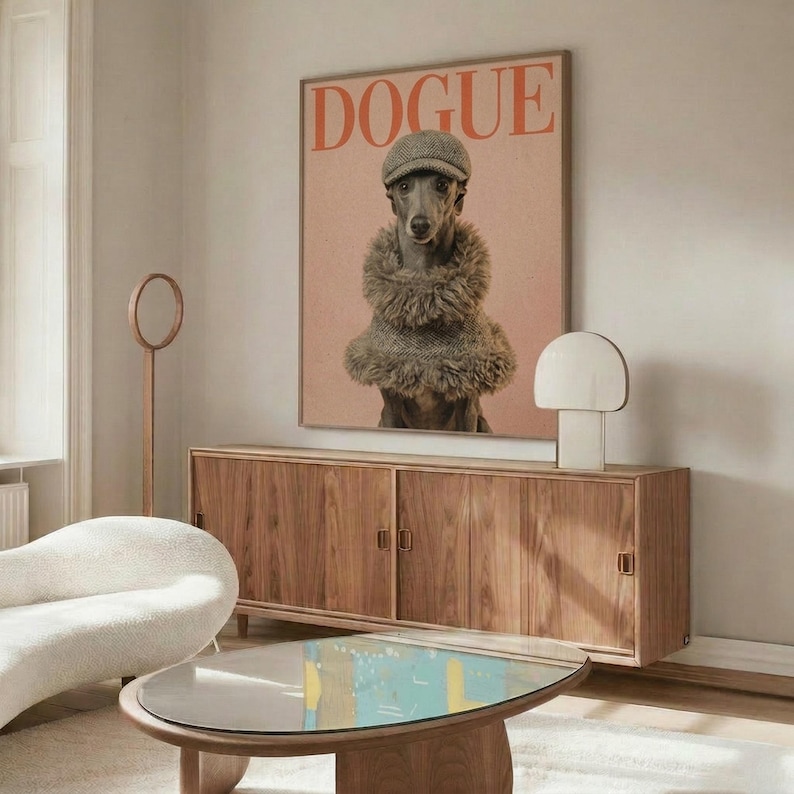 May include: Framed poster featuring a whippet dog wearing a knitted cap and furry collar on pink background with "DOGUE" text in red letters, displayed above wooden mid-century credenza in modern living room with white curved chair, oval glass coffee table, and white table lamp