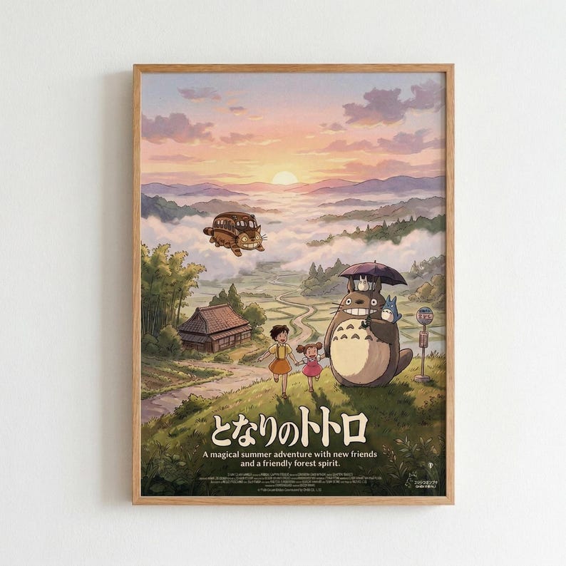 May include: Framed Studio Ghibli poster mounted on white wall showing Totoro characters in pastoral countryside scene. Two children stand beside large gray forest spirit holding umbrella, with flying cat bus in cloudy sky above. Warm sunset colors of pink, orange and purple fill the background mountains. Japanese text and English subtitle appear at bottom. Light wood frame surrounds the colorful anime-style artwork.