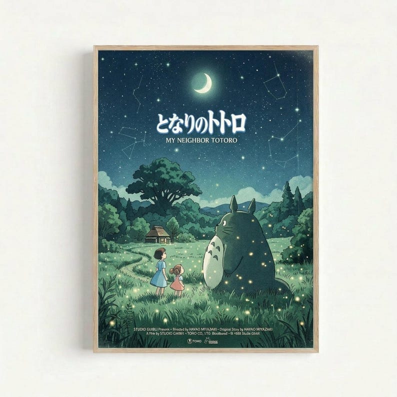Framed poster featuring Totoro and two children in a moonlit meadow scene. The artwork shows a large gray forest spirit sitting beside two young girls against a starry night sky with crescent moon and constellation patterns. Rolling green hills, trees, and a small house create the pastoral landscape background. The image has a dreamy, animated film aesthetic with soft blues and greens. Japanese text appears at the top with English translation below. Studio credits are visible at the bottom of th