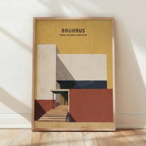 Puede incluir: Lámina enmarcada de arte Bauhaus con un diseño arquitectónico geométrico. La obra de arte muestra un edificio con una fachada roja, beige y blanca, una escalera y el texto "BAUHAUS" y "FORM FOLLOWS FUNCTION". La impresión está en un marco de madera.