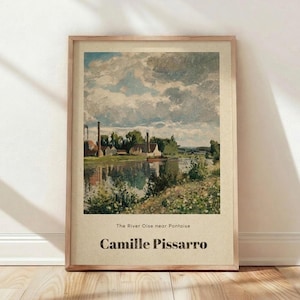 May include: Framed art print of a landscape painting by Camille Pissarro. The artwork depicts a river scene with buildings, trees, and a cloudy sky. The text "The River Oise near Pontoise" and the artist's name are at the bottom.