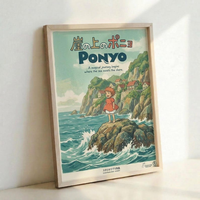 May include: Framed Ponyo movie poster in light wood frame leaning against white wall. Features anime girl with orange hair in red dress standing on rocky outcrop with ocean waves splashing around. Coastal village with houses on green cliffs in background under soft blue-green sky. Japanese text at top with "PONYO" in large dark letters and tagline below. Studio Ghibli artwork in watercolor illustration style with vintage poster aesthetic.