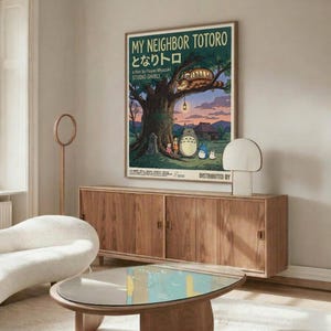 May include: Vintage-style My Neighbor Totoro movie poster displayed above a mid-century walnut credenza in a minimalist living room. The colorful poster shows Totoro characters beneath a large tree with the Catbus above. Room features a white curved chair, glass coffee table, and warm natural lighting creating shadows on pale walls.