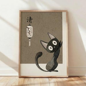 May include: A framed poster print leaning against a white wall on light wooden flooring. The artwork features a stylized black cat with large white eyes sitting upright, rendered in a textured, crackled art style. Above the cat is a white paper lantern with cherry blossom branches and Japanese characters. The background has an olive-green, aged appearance with visible crack textures. The print is displayed in a thin wooden frame with natural wood tones.