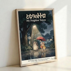 May include: Framed poster featuring My Neighbor Totoro movie artwork displayed against a white wall. The poster shows children with umbrellas meeting Totoro at a rainy bus stop under large trees, rendered in Studio Ghibli's distinctive animated style with deep blues and greens. Japanese text appears at the top with English title below. Natural wood frame surrounds the artwork.
