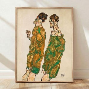 May include: Framed print of an abstract artwork featuring two figures in draped garments. The figures are rendered in shades of gold and green, with visible brushstrokes and a textured appearance. The artwork is set against a neutral background and framed in a light wood.